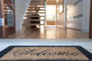 Close up of a welcome mat in front of an inviting house. Focus on foreground.
